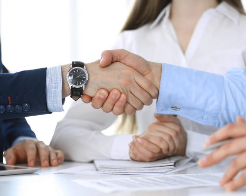 Business people shaking hands at meeting or negotiation, close-up. Group of unknown businessmen and women in modern office. Teamwork, partnership and handshake concept.